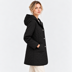 A woman wearing a black quilted hooded coat with silver buttons, shown from a side profile against a light gray studio background.