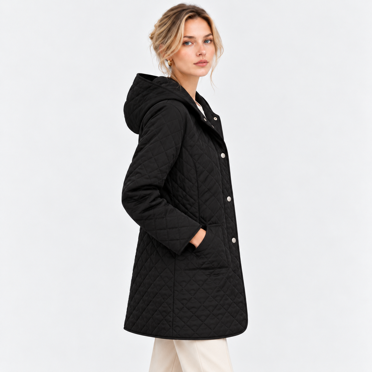 A woman wearing a black quilted hooded coat with silver buttons, shown from a side profile against a light gray studio background.