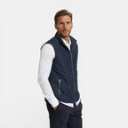 Man wearing a navy vest over a white shirt on a light gray background