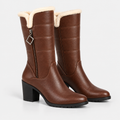 A pair of brown faux-leather mid-calf boots with a cream sherpa lining at the top, a side zipper with a diamond-shaped pull tab, and a chunky black block heel, shown on a light gray background.