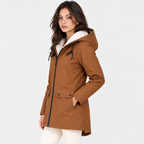 A woman modeling a brown hooded parka jacket with a white sherpa lining, shown from the waist up against a plain light gray studio background.