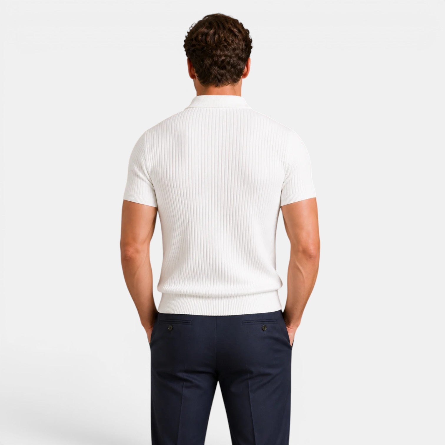 Back view of a man wearing a white ribbed knit polo shirt with navy trousers against a light gray background.
