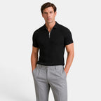 Man wearing a black ribbed knit polo shirt with gray trousers, standing against a light gray background.