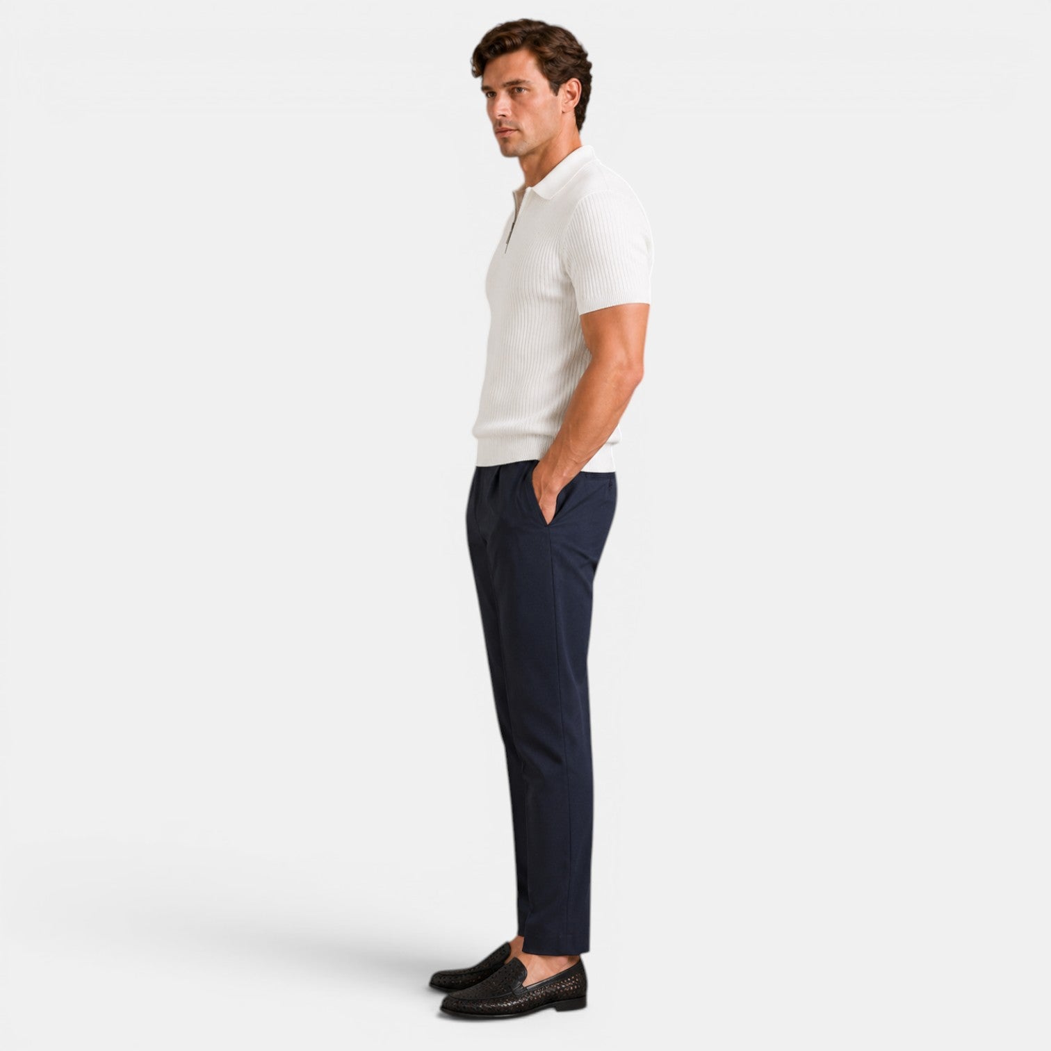 Side view of a man wearing a white ribbed knit polo shirt with navy trousers and dark loafers.