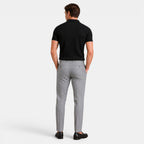 Back view of a man wearing a black ribbed knit polo shirt with gray trousers and black loafers.