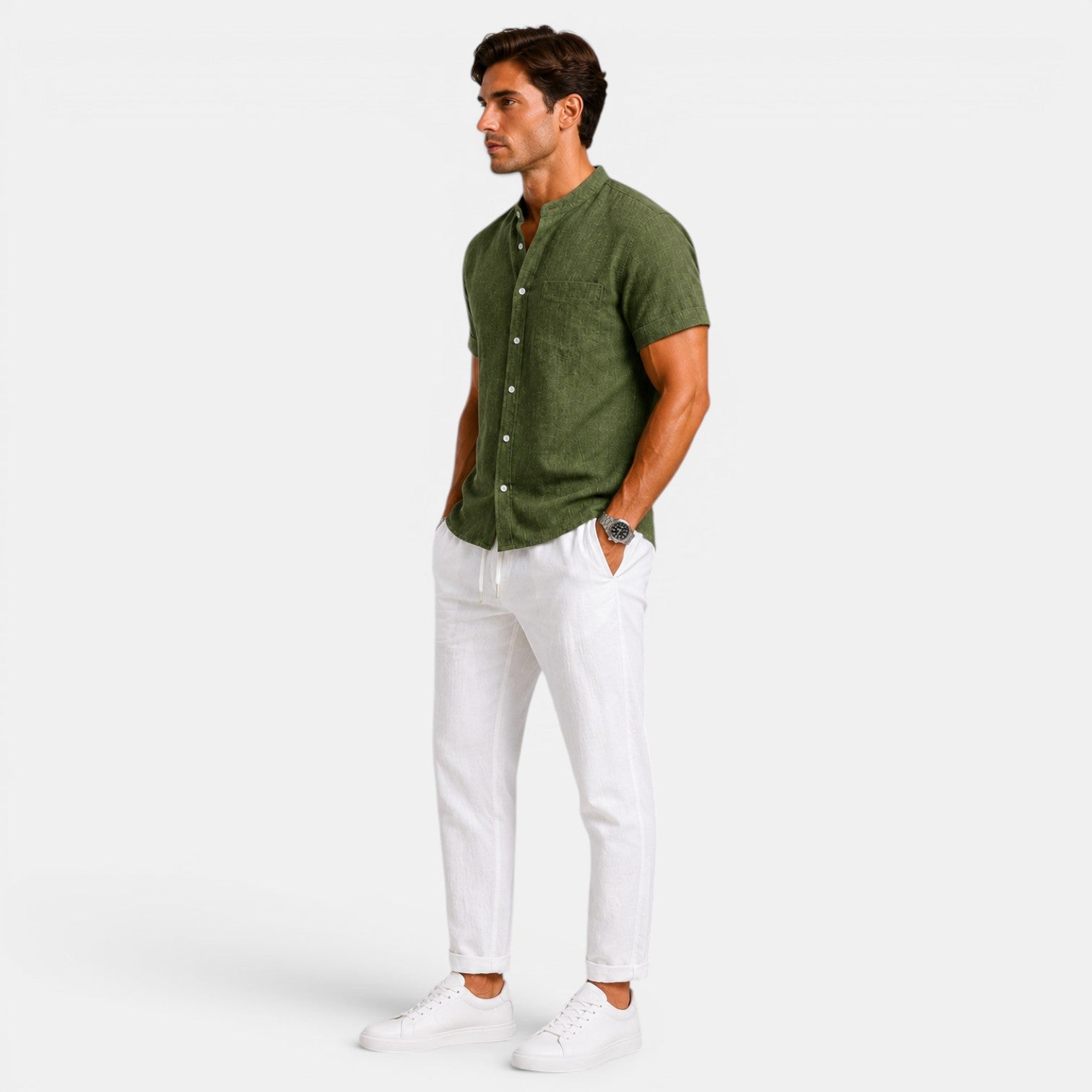 Side view of a man wearing an olive green short-sleeve button-up shirt with white drawstring trousers and white sneakers against a light gray background.