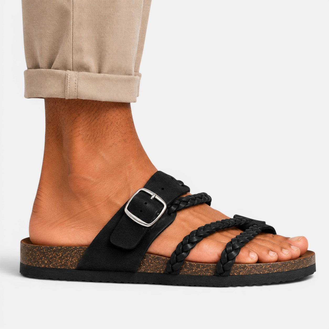 Black braided strap sandal with an adjustable buckle and cork-style footbed, worn with rolled beige trousers.