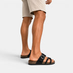 Black braided strap sandals with adjustable buckles, worn with beige shorts from a rear side view.