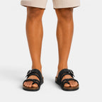 Front view of black braided strap sandals with adjustable buckles, worn with beige shorts.