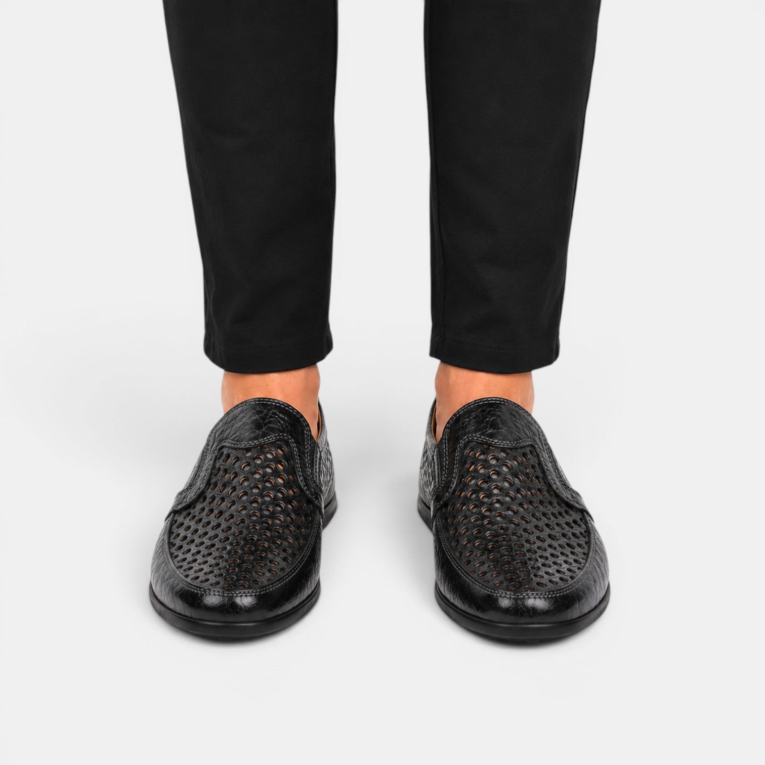 Black perforated leather loafers worn with black trousers, shown from the front.