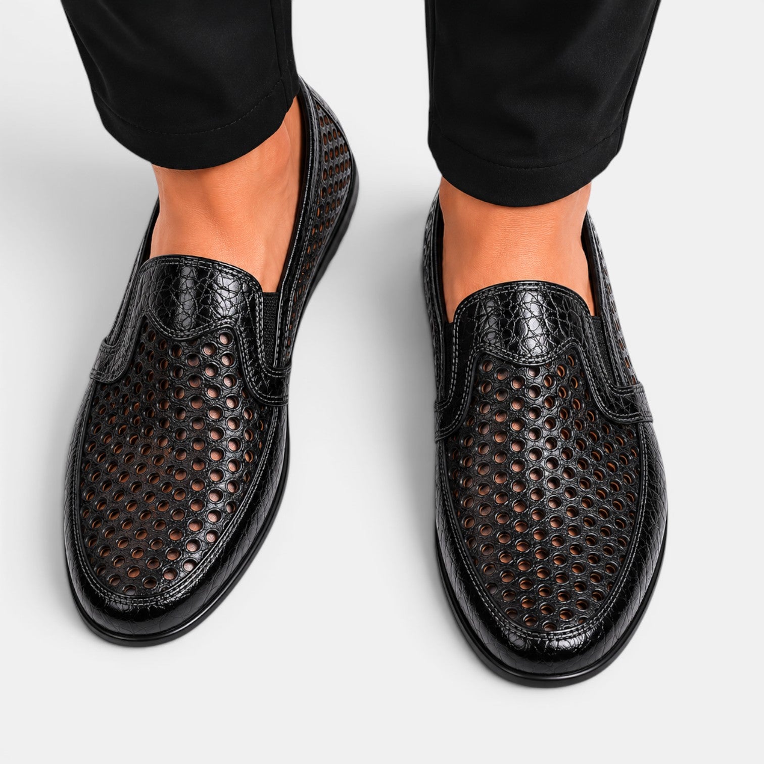 Top view of black perforated leather loafers with a breathable slip-on design, worn with black trousers.