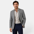 Young man wearing a checked blazer, beige dress shirt, and navy trousers.