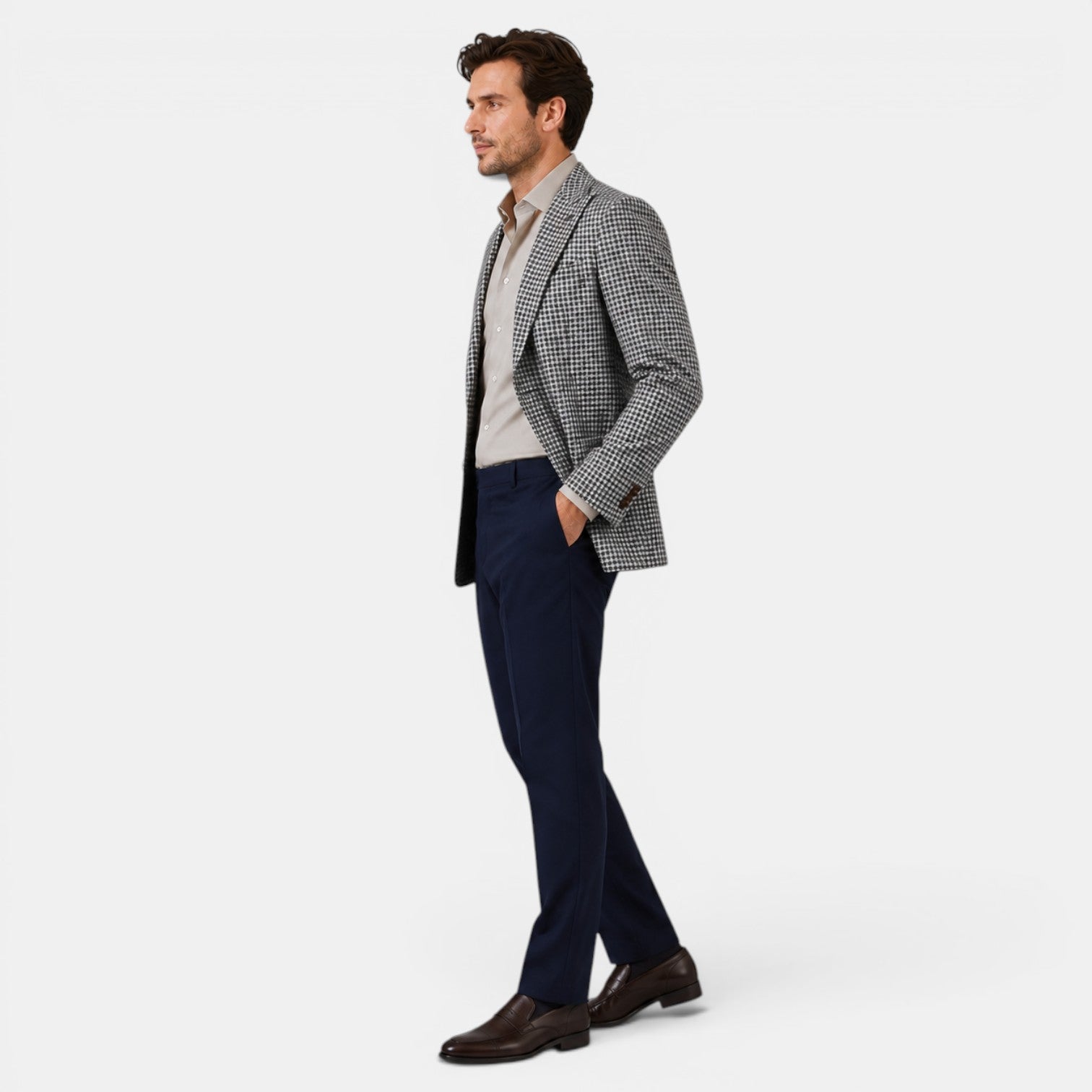 Full-length side view of a young man wearing a checked blazer, beige dress shirt, navy trousers, and brown loafers.