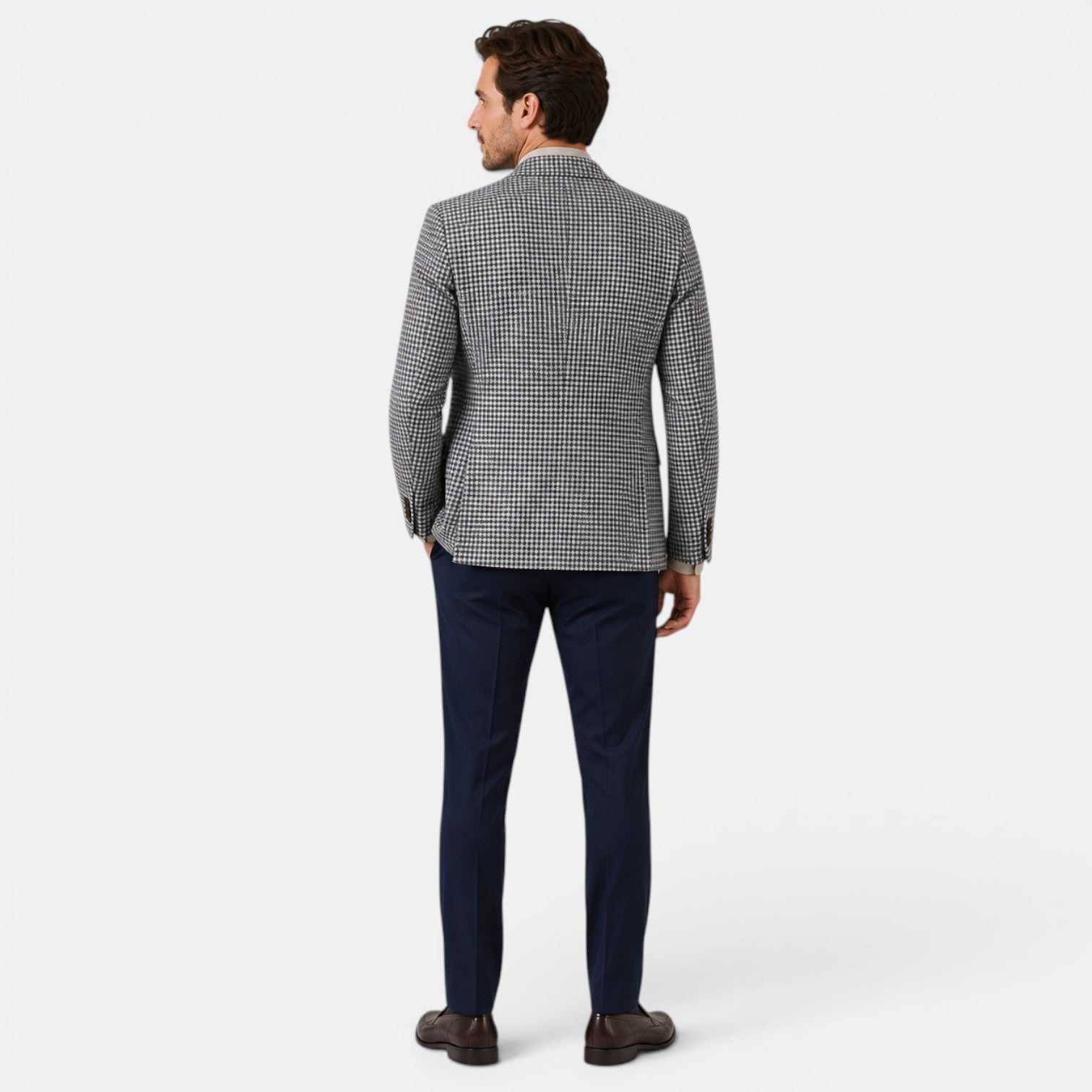 Back view of a young man wearing a checked blazer, navy trousers, and brown loafers.