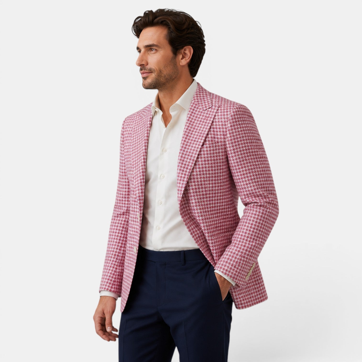 Side view of a young man wearing a pink checked blazer, white dress shirt, and navy trousers.