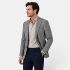 Side view of a young man wearing a checked blazer, beige dress shirt, and navy trousers.