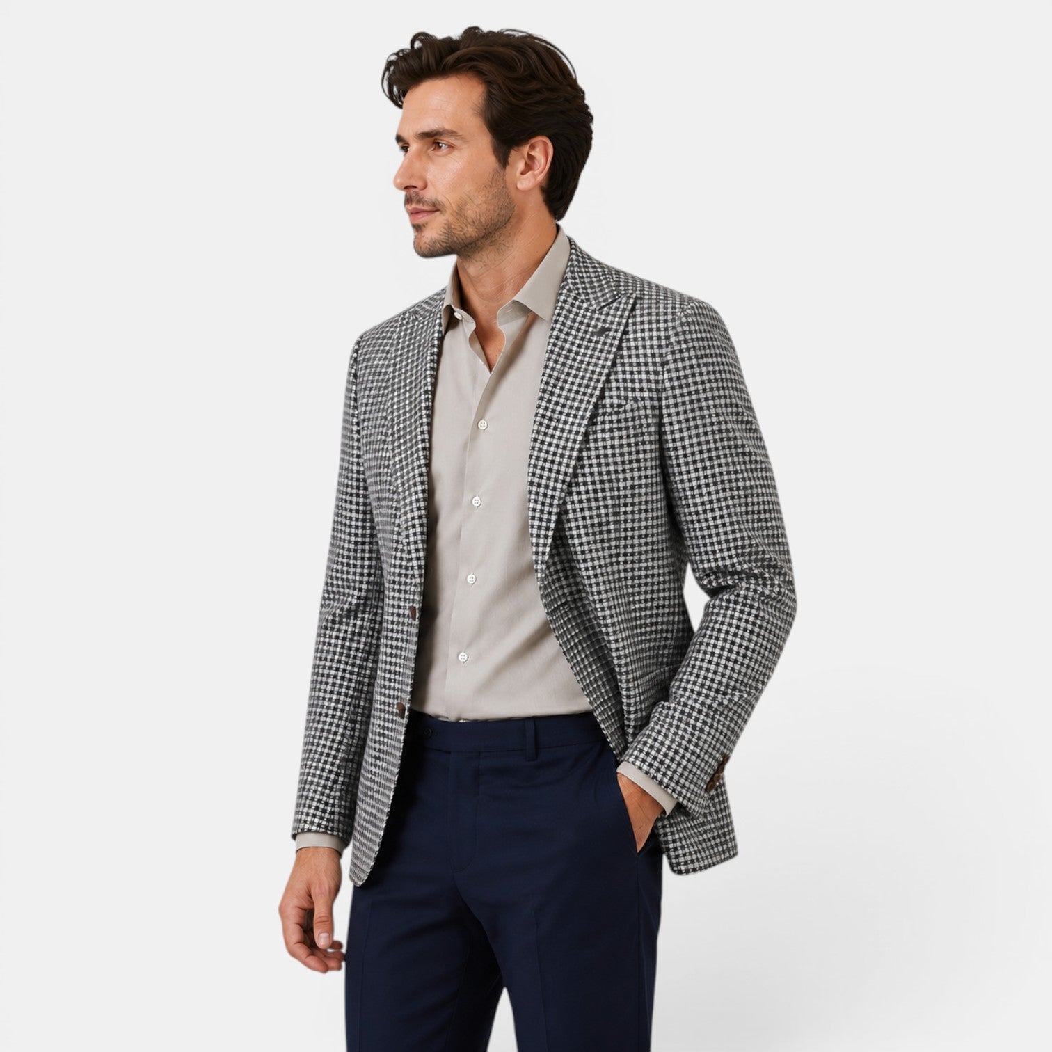 Side view of a young man wearing a checked blazer, beige dress shirt, and navy trousers.