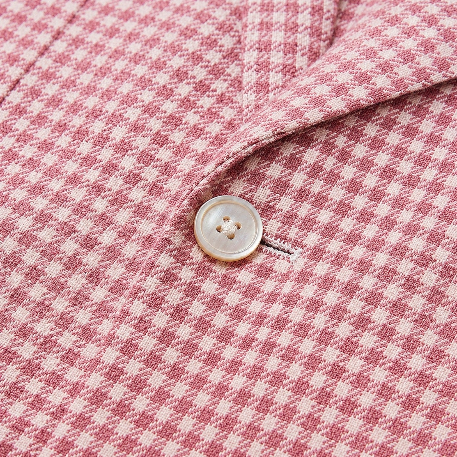 Close-up of a pink houndstooth blazer featuring textured fabric and a classic button detail.
