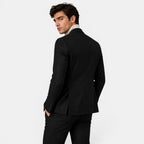 Back view of a young man wearing a black suit and cream turtleneck sweater.