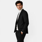 Side view of a young man wearing a black suit and cream turtleneck sweater.