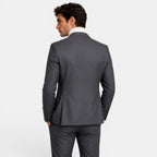 Back view of a young man wearing a charcoal gray suit and cream turtleneck sweater.