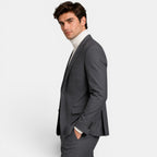Side view of a young man wearing a charcoal gray suit and cream turtleneck sweater.