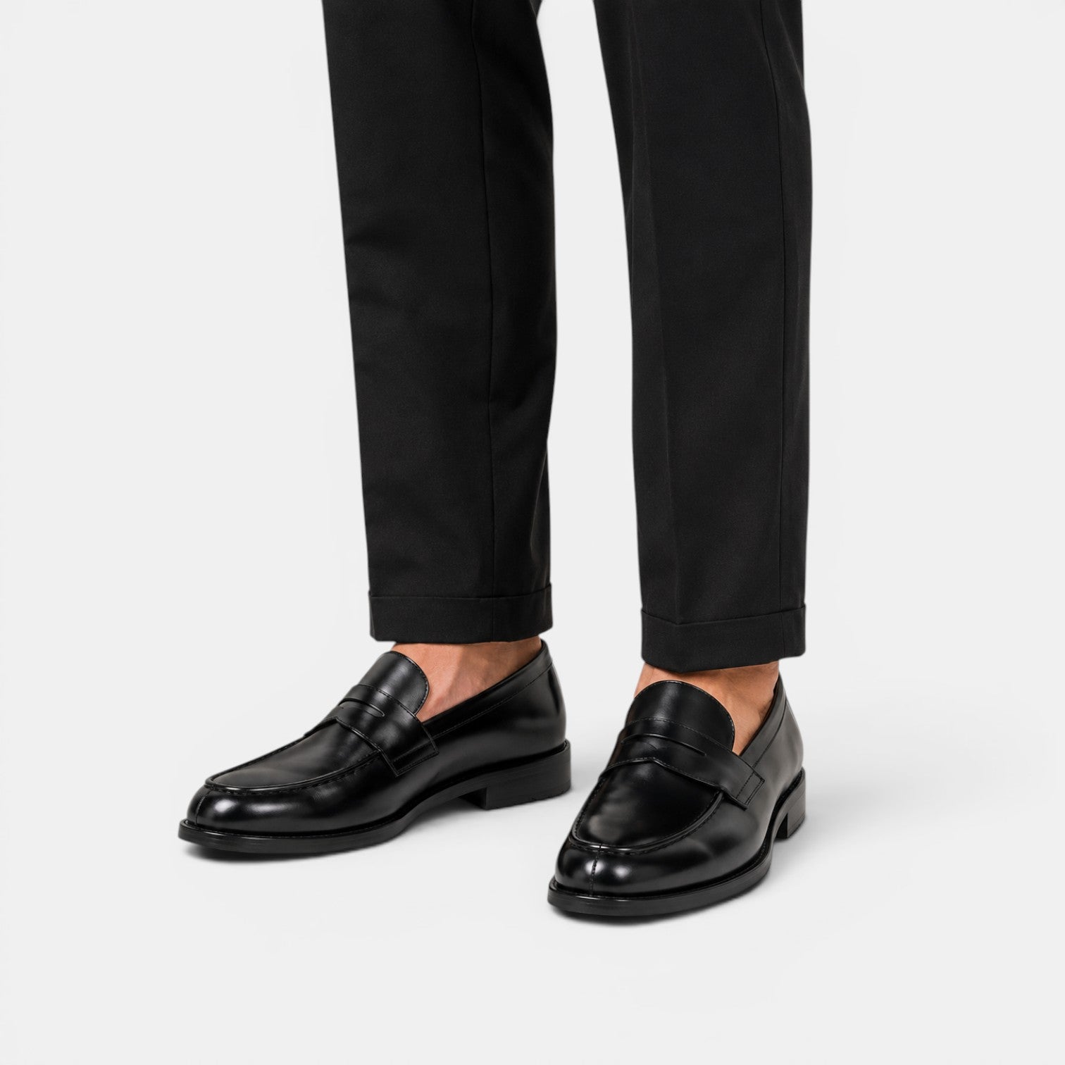 Black loafers worn with black pants on a white background