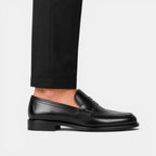 Black leather loafer worn with black pants on a light gray background