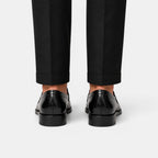 Black dress shoes worn with black pants on a white background