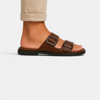 Brown sandal with buckles worn by a person on a white background