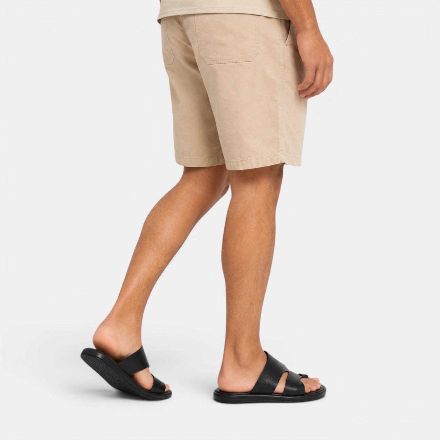 Person wearing beige shorts and black sandals on a white background