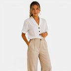 Woman wearing a white blouse with buttons and beige pants on a light background