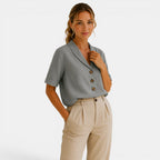 Woman wearing a gray short-sleeve blouse with buttons and beige pants on a white background