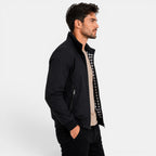 Man wearing a black jacket over a checkered shirt on a white background
