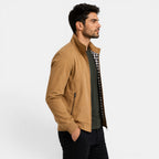 Man wearing a tan jacket over a plaid shirt on a white background