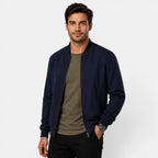 Man wearing a navy bomber jacket over a green shirt on a white background