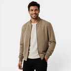 Man wearing a beige bomber jacket over a white shirt on a light gray background