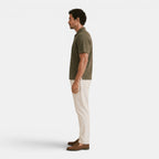 Side view of a man wearing an olive green textured knit polo shirt, cream trousers, and brown loafers against a light gray background.