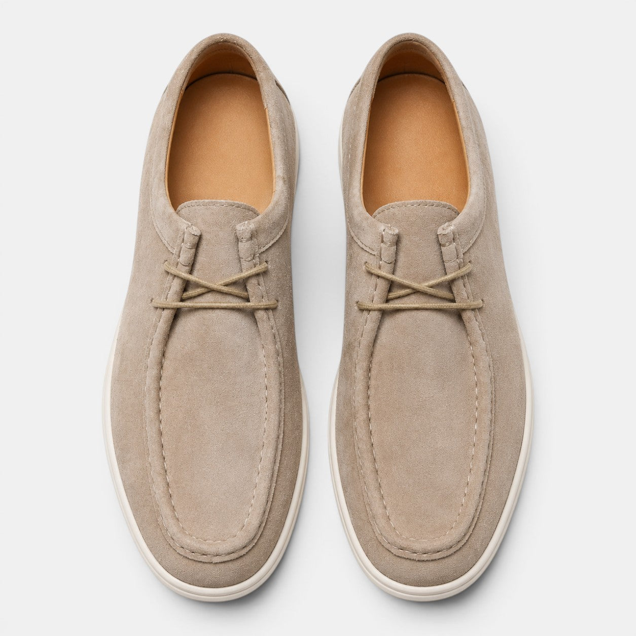 Top view of a pair of beige suede lace-up shoes with white soles against a light gray background.