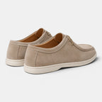 Rear angled view of a pair of beige suede lace-up shoes with white soles against a light gray background.