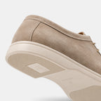 Close-up view of a beige suede lace-up shoe with a white rubber sole, highlighting the textured upper and outsole details.