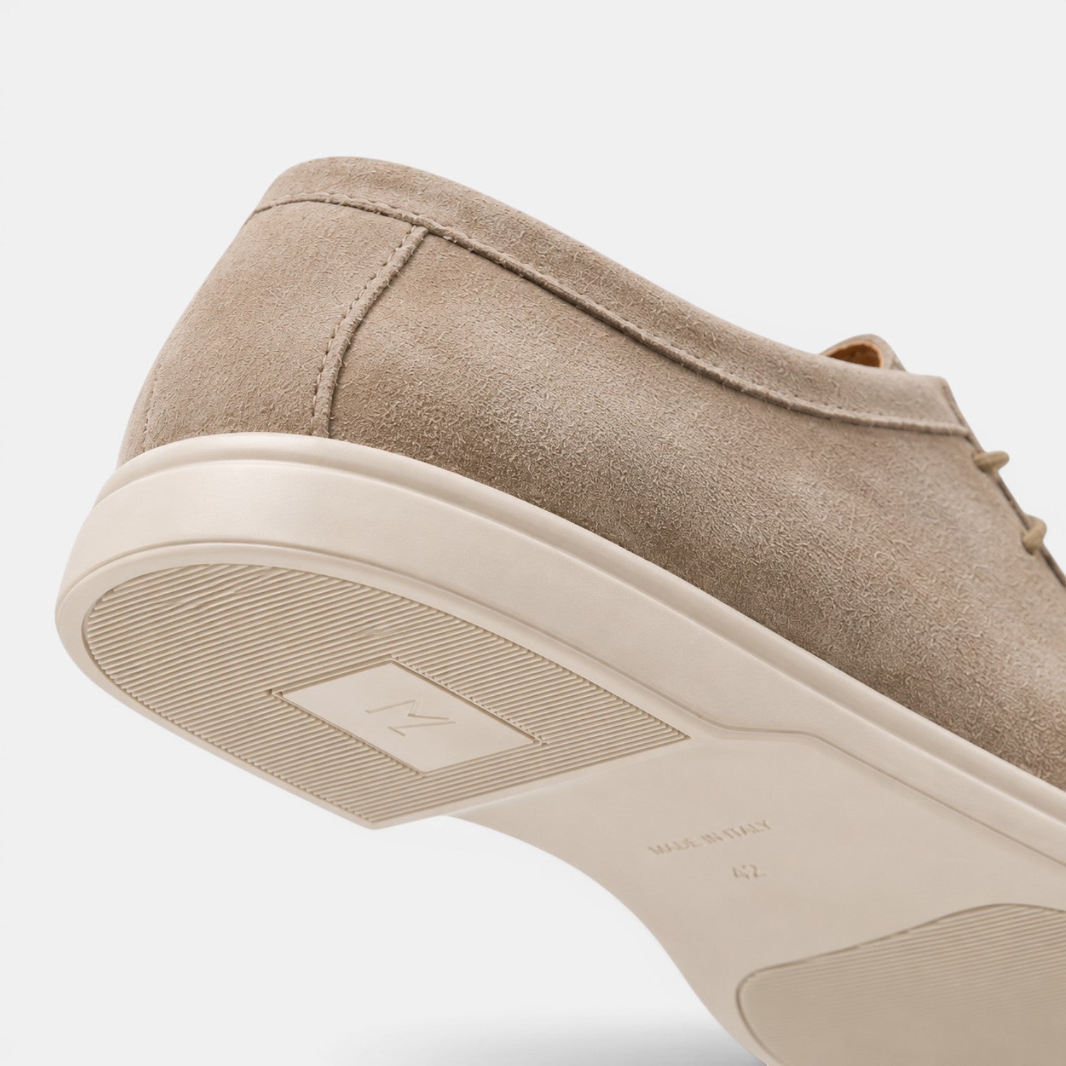 Close-up view of a beige suede lace-up shoe with a white rubber sole, highlighting the textured upper and outsole details.