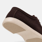 Close-up view of a dark brown suede lace-up shoe with a white rubber sole, highlighting the textured upper and outsole details.