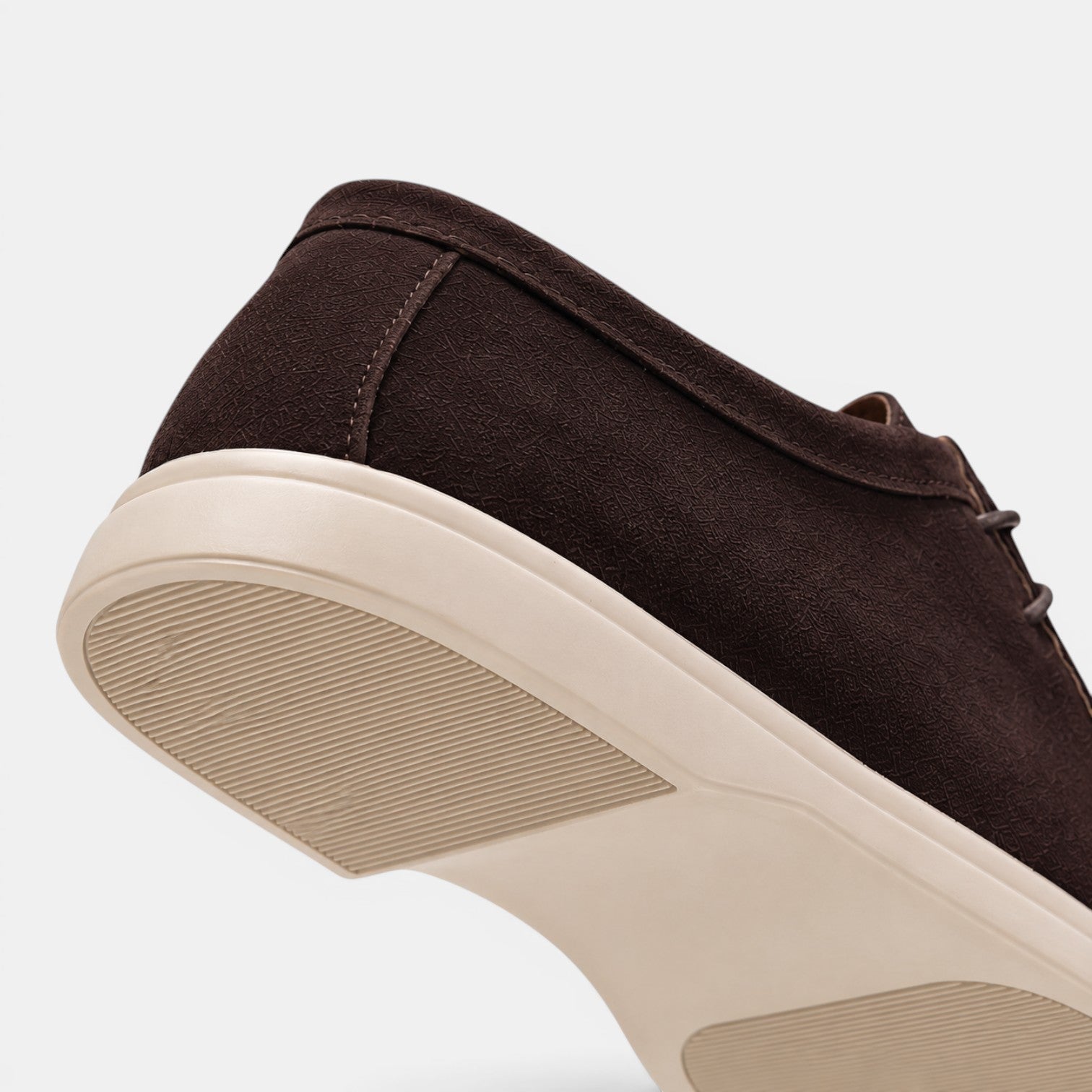 Close-up view of a dark brown suede lace-up shoe with a white rubber sole, highlighting the textured upper and outsole details.