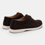 Rear angled view of a pair of dark brown suede lace-up shoes with white soles against a light gray background.
