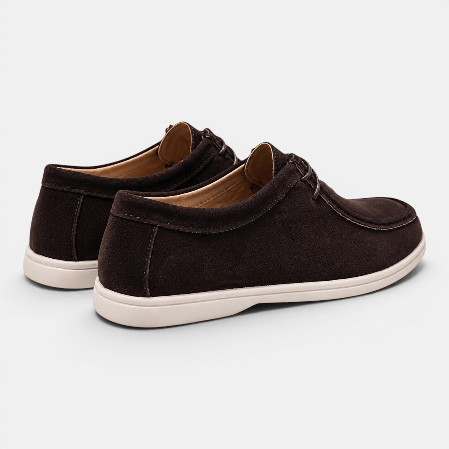 Rear angled view of a pair of dark brown suede lace-up shoes with white soles against a light gray background.