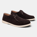Pair of dark brown suede lace-up shoes with white soles, displayed against a light gray background.