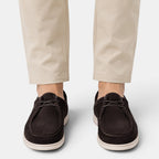 Person wearing dark brown suede lace-up shoes with white soles and beige trousers, viewed from the front.