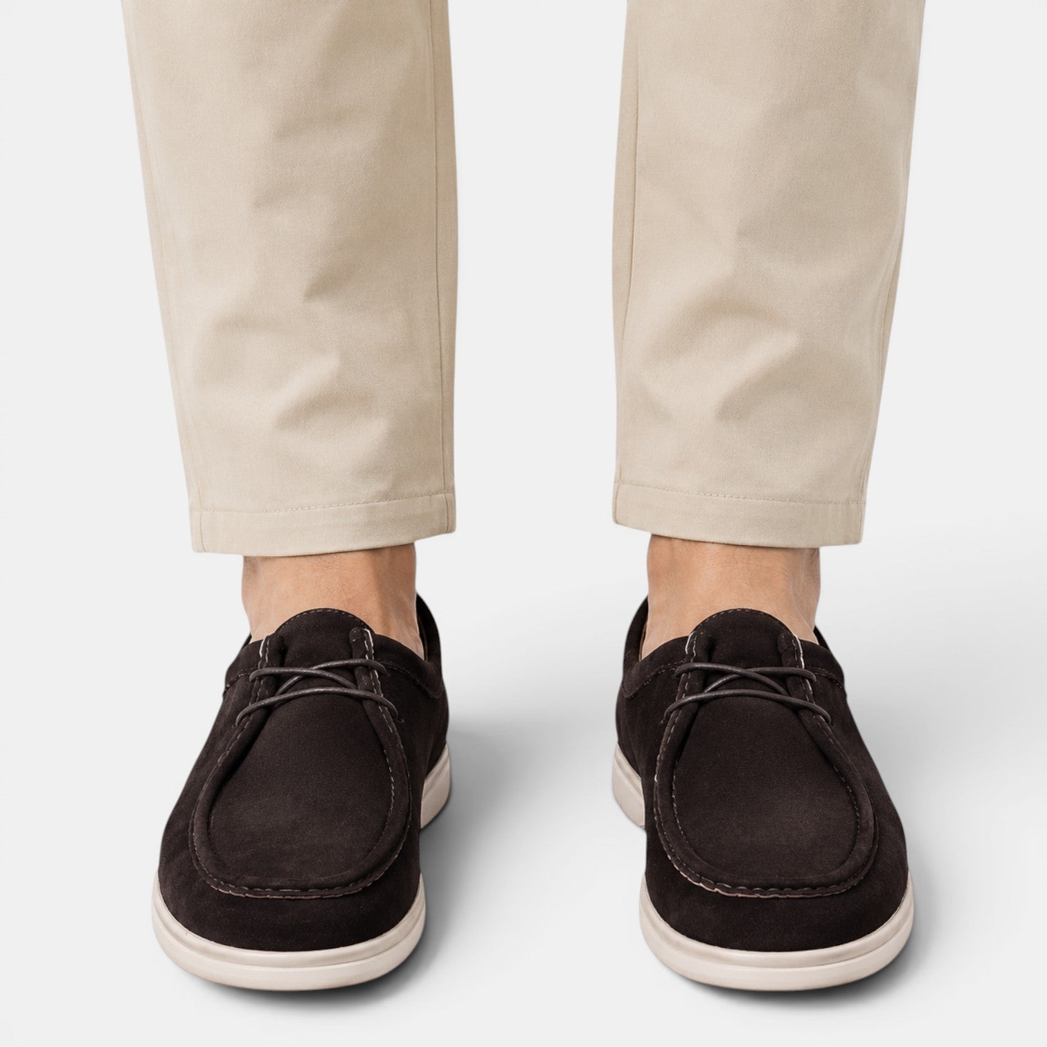 Person wearing dark brown suede lace-up shoes with white soles and beige trousers, viewed from the front.