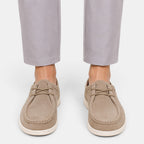 Person wearing beige suede lace-up shoes with white soles and light gray trousers, viewed from the front.